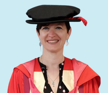 Dr Frederique (Fred) Bouilheres wearing a red graduation gown and black hat in front of a pale blue background
