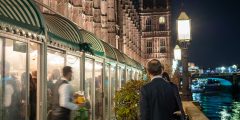 People standing outside a glass building attached to the House of Commons at night with Big Ben in the background