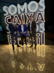 Meryem Duygun wearing a blue jacket standing in front of a brightly lit sign - SOMOS CAIXA SOMOS Brasil at The Caixa Econômica Federal