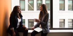 Two women talking on a window ledge in an office building.