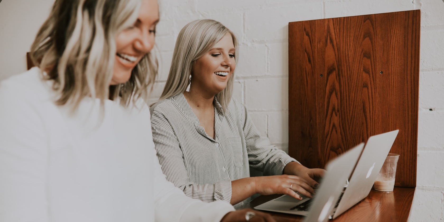 Two women at working on laptops but laughing.