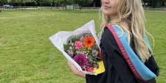 Profile picture of liberal arts graduate, Zoe, in graduation robes holding some flowers.