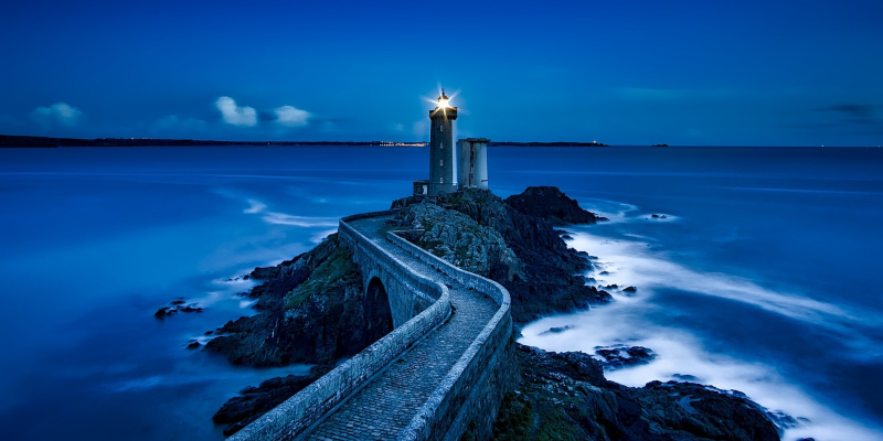 Lighthouse in the evening with a light shining and a walled road leading to it