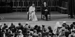 Photograph of two people on a stage in front of a seated crowd