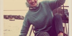Woman wearing headscarf, jumper and deck shoes, sitting on the deck of a yacht