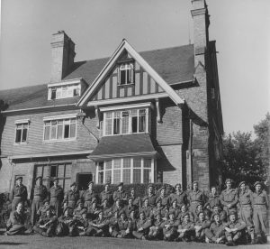 Black and white photograph of a group of men in military uniform in front of a large house.