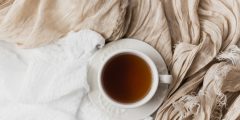 A ceramic cup and saucer of tea rest on a white bedspread